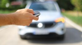 Hand hält einen Autoschlüssel vor einem unscharfen weißen Mercedes
