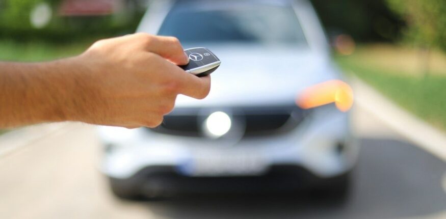 Hand hält einen Autoschlüssel vor einem unscharfen weißen Mercedes