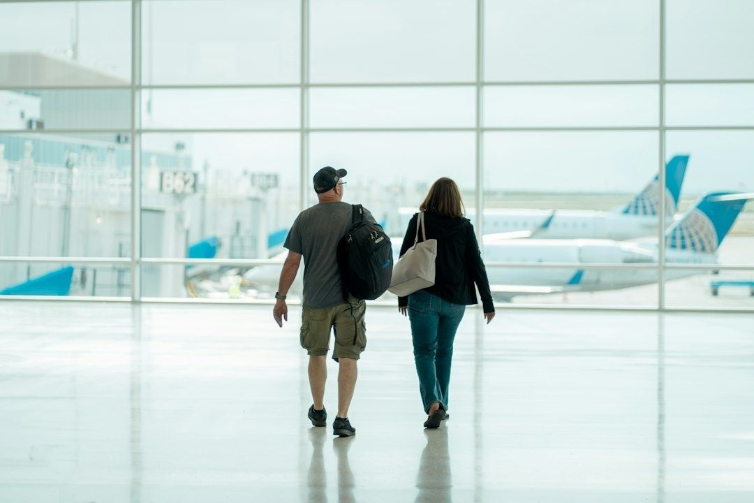 Zwei Reisende mit Rucksack und Tasche gehen durch einen hellen Flughafen